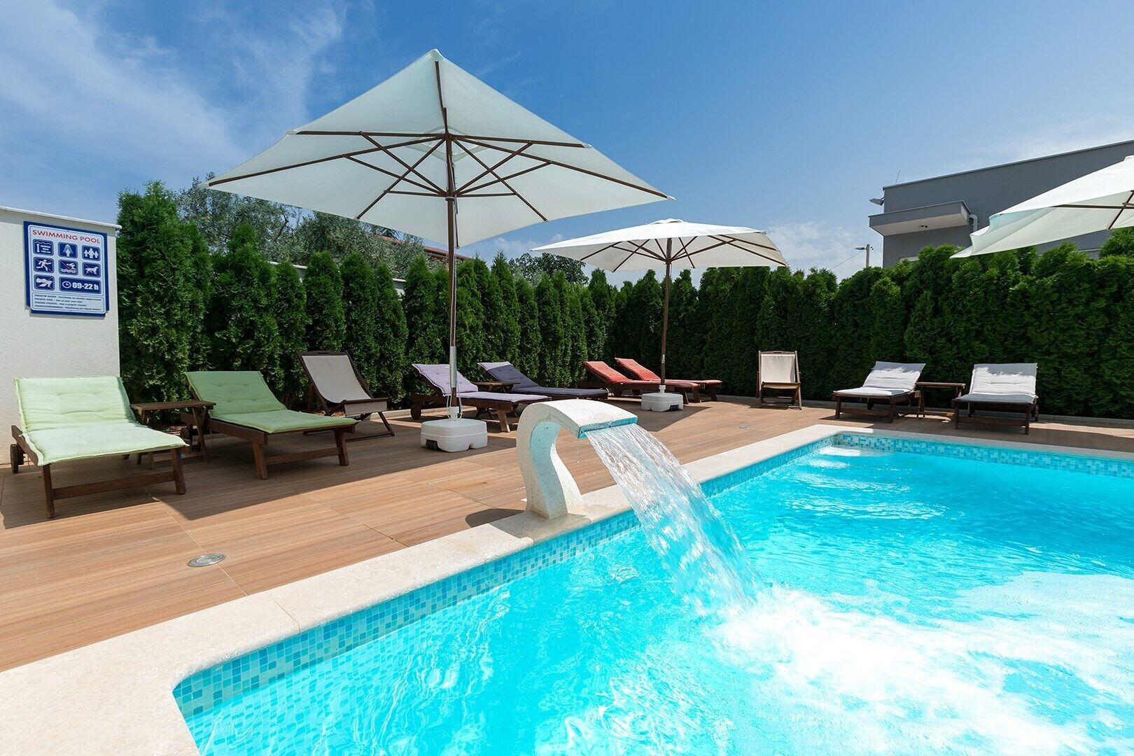 A swimming pool with lounge chairs and umbrellas, surrounded by greenery.