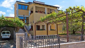 A two-story building with a yellow facade, a covered outdoor area with a pergola, and a car parked in a driveway. - Popular fully equipped modern one bedroom apartment in a top location in Porec near the beach (Porec)