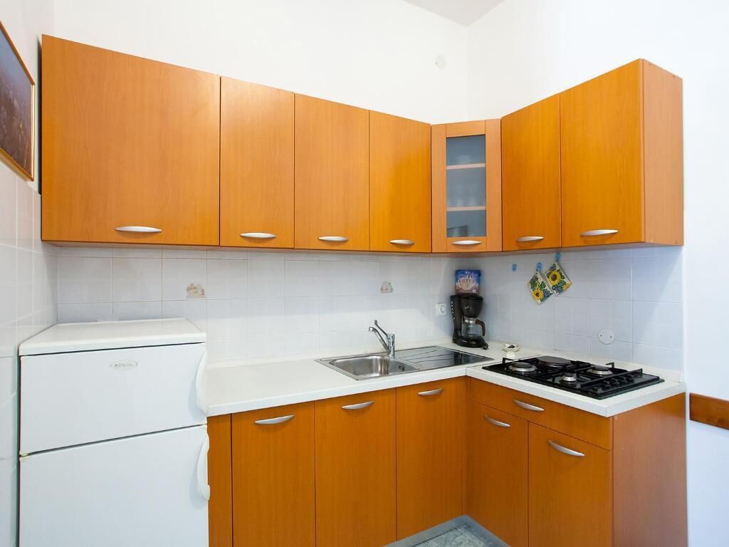 Una cocina compacta con armarios de madera, una encimera blanca, estufa, fregadero y refrigerador.
