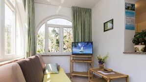 A living room with a sofa, a television on a stand, a small table, and a window with curtains. - Popular fully equipped modern one bedroom apartment in a top location in Porec near the beach (Porec)