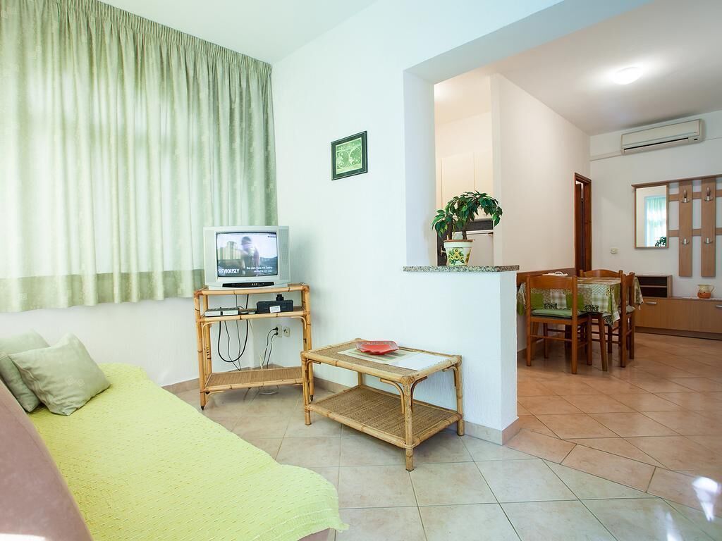 Ein Wohnzimmer mit einer Couch, einem Fernseher, einem kleinen Tisch und einem Essbereich mit Stühlen.