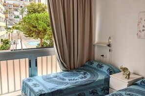Ein Schlafzimmer mit einem Bett mit gemusterten Bettwaren, einem Nachttisch mit Lampe und Blick auf einen Pool sowie Gebäude im Freien.