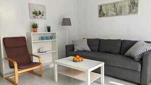 A living room with a grey sofa, a brown chair, a white coffee table with oranges, a floor lamp, and a wall with a Buddha painting. - SAN ANGELO Levante beach apartments (Benidorm)