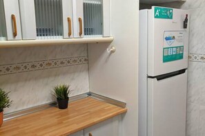 A kitchen with a wooden countertop, a refrigerator with a sticker, and cabinets with glass doors.