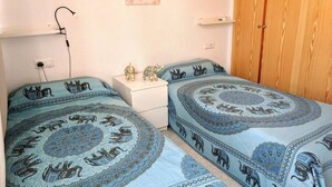 Ein Schlafzimmer mit zwei Betten, einem Nachttisch, einem Holzschrank und einem an der Wand befestigten Regal.