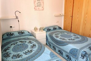 Une chambre avec deux lits, une table de chevet, une armoire en bois et une étagère fixée au mur.