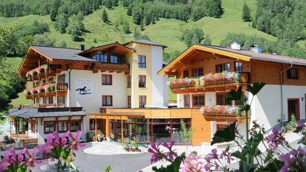 A hotel with multiple balconies adorned with flowers, set against a backdrop of green hills. - Pferdegut Romerhof (Altenmarkt im Pongau)
