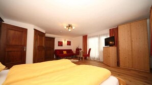 A hotel room with a large bed, wooden wardrobe, a TV, and a red sofa. - Pferdegut Romerhof (Altenmarkt im Pongau)