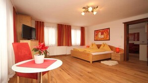 A bedroom with a wooden bed, a red chair, a small table with a plant, and a television on a wooden cabinet. - Pferdegut Romerhof (Altenmarkt im Pongau)