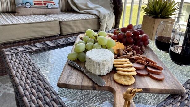 Ein Holzbbrett mit Käse, Trauben, Crackern und Schinken auf einem Tisch.