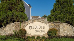 Ein Steinschild mit der Aufschrift "REHOBOTH CROSSING", umgeben von Grünpflanzen und Bäumen.