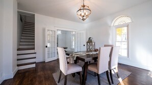 A dining room with a wooden table, four upholstered chairs, a chandelier, and a staircase. - Beautifully renovated 3,800 sq ft house between 2 federal lakes  (Lyndon)