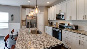 Una cocina con encimeras de granito, armarios blancos, electrodomésticos de acero inoxidable e iluminación colgante.