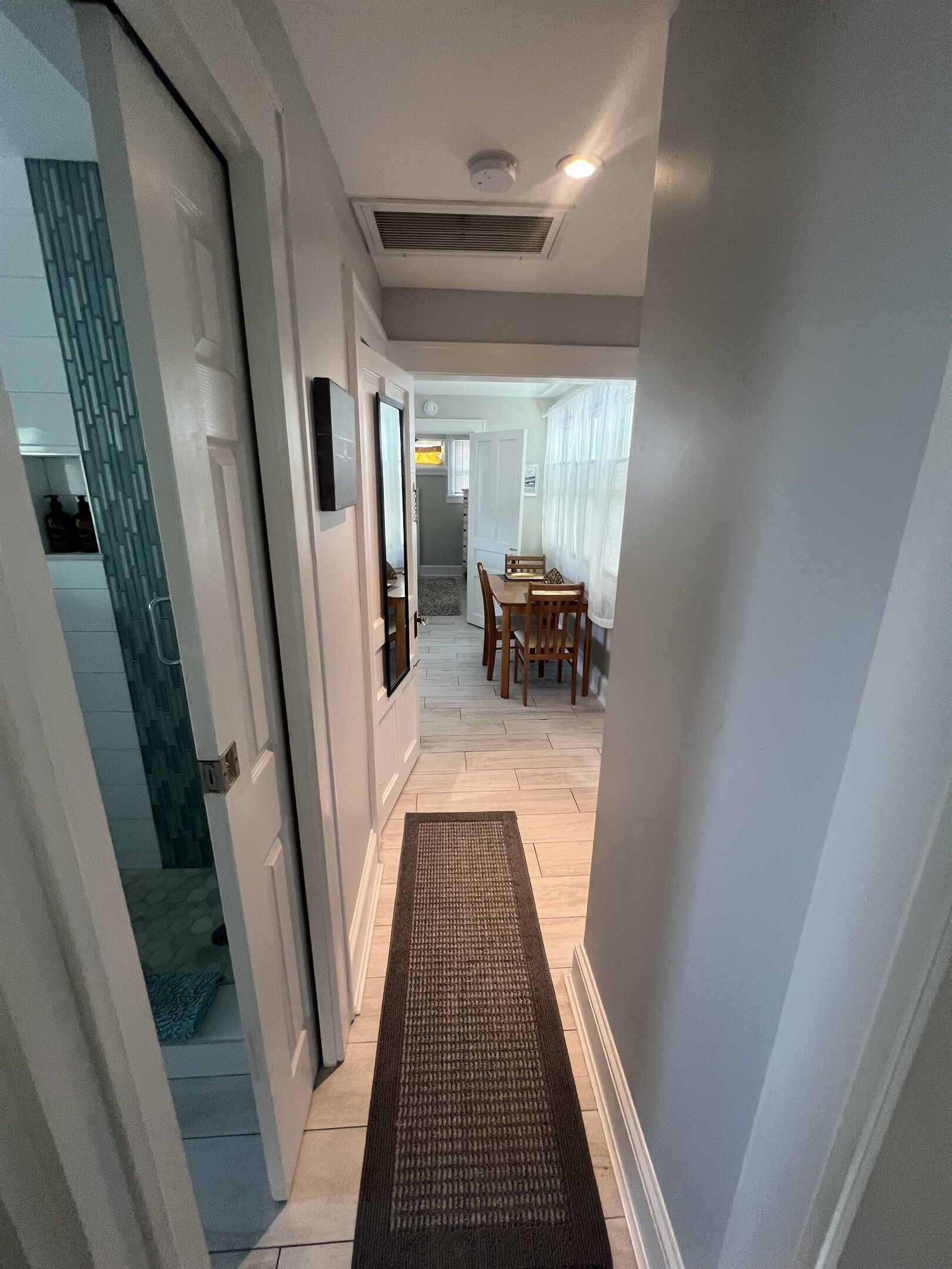 A hallway leading to a dining area with a rug, a ceiling vent, and a door.