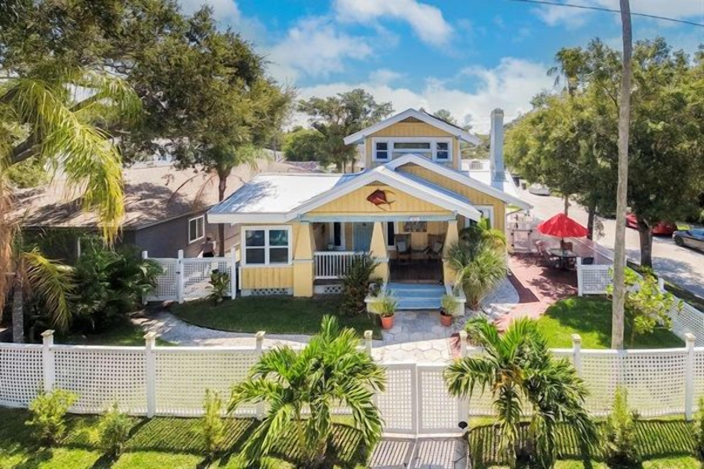 A two-story house with a front porch, a red umbrella, and a white picket fence.