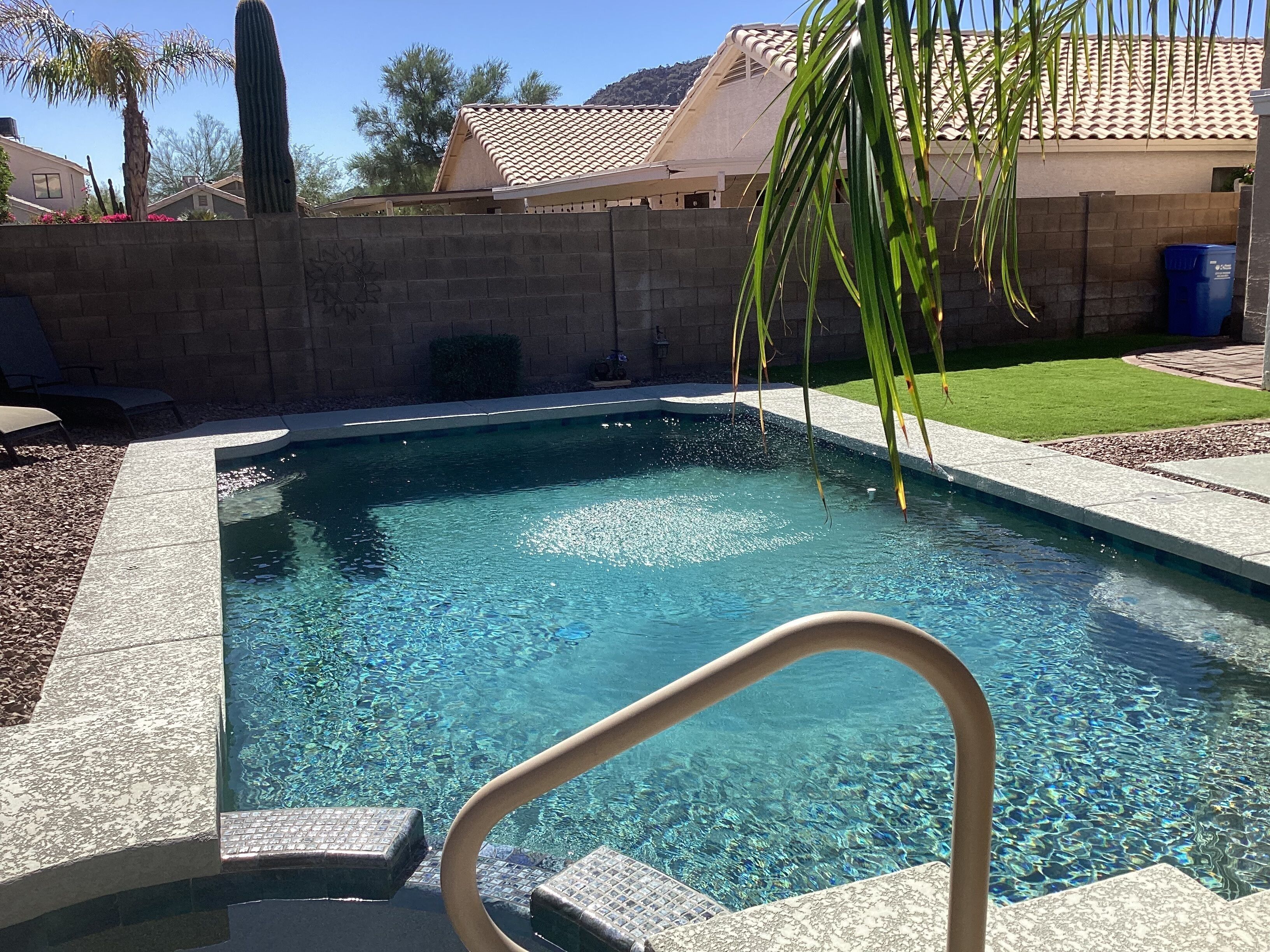 A clear swimming pool with a tiled edge, surrounded by a brick wall and a grassy area.