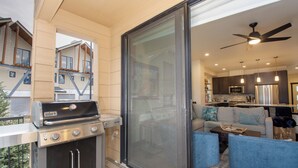 A modern kitchen with a built-in oven, a dining area with a blue sofa, and a sliding glass door leading to a balcony with a barbecue grill. - Arrow at Winter Park Unit 248 Downtown 4 bedroom private hot tub & mountain view (Winter Park)