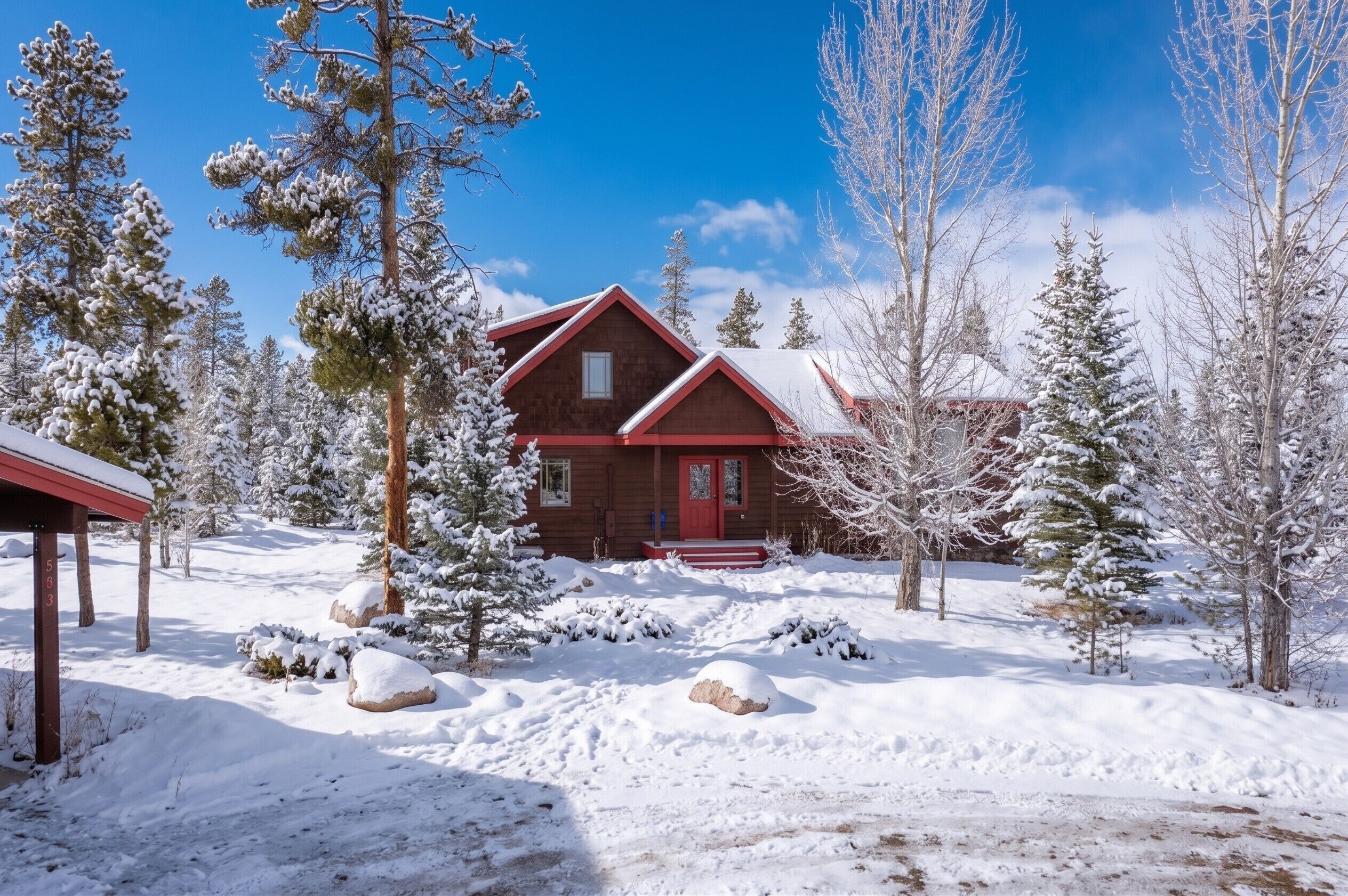 A cabin with a red door, surrounded by snow-covered trees and rocks.