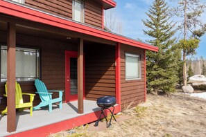 A two-story wooden house with a red exterior, a porch with two Adirondack chairs, and a barbecue grill. - Cabin getaway 3 bedroom, garage, open floor plan (Fraser)