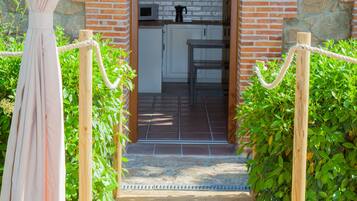Una terraza de madera que conduce a una entrada de ladrillo, con una cocina visible en el interior.