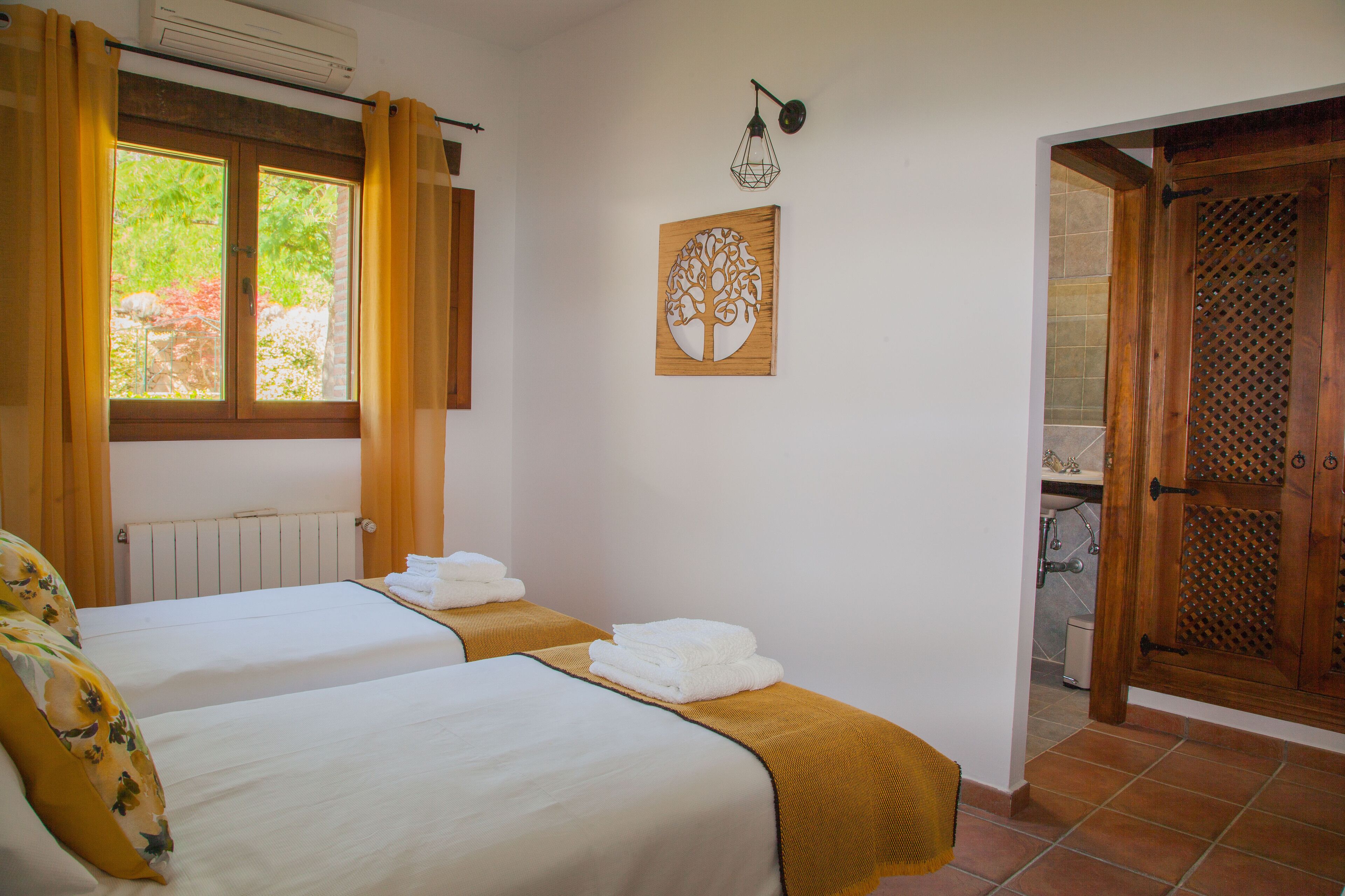 Una habitación de hotel con dos camas, un radiador, una ventana con cortinas, una lámpara fijada a la pared y una puerta de madera.