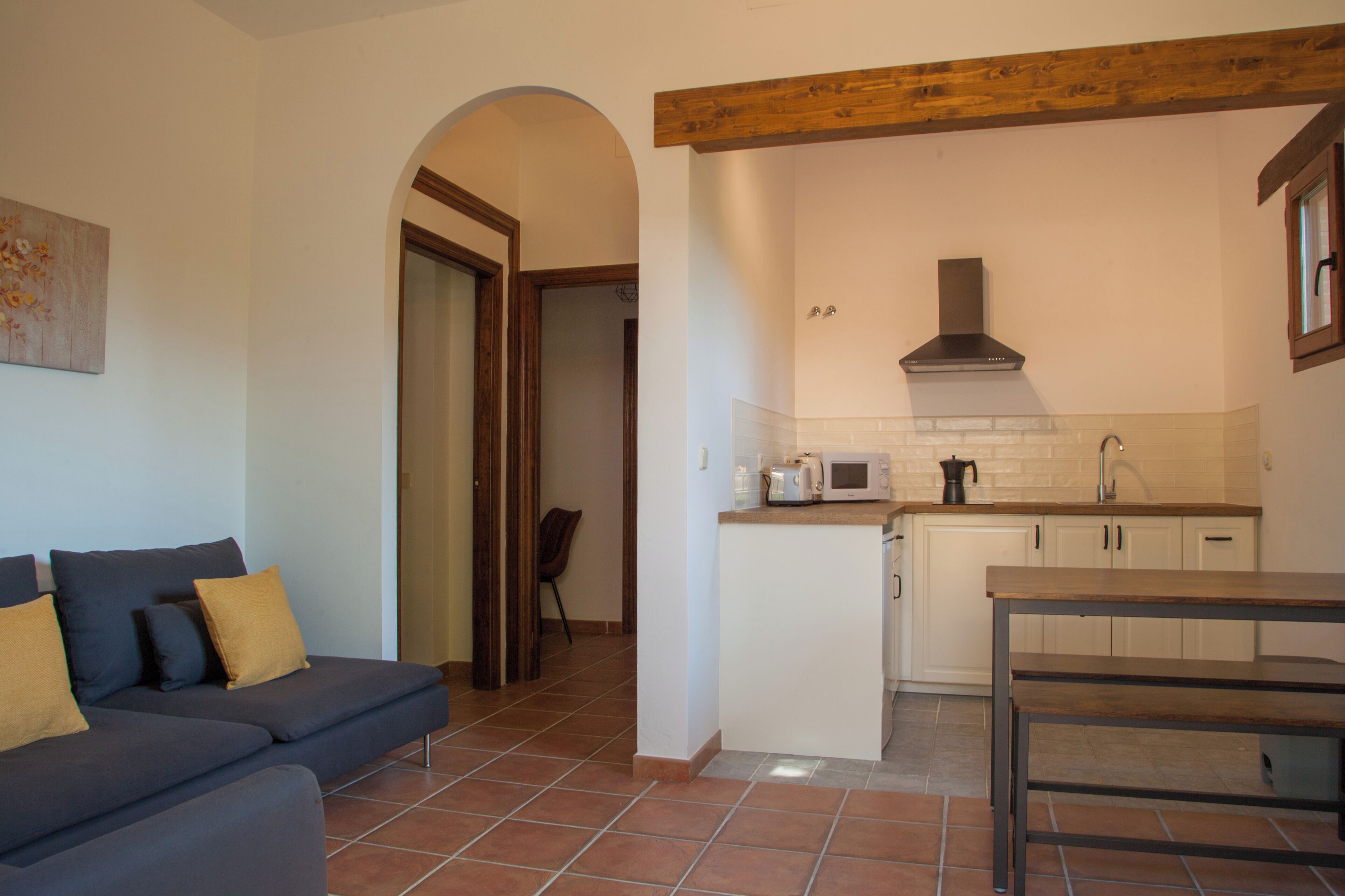 Un espacio habitable compacto con kitchenette, un sofá con cojines, una mesa de comedor y una viga de techo de madera.