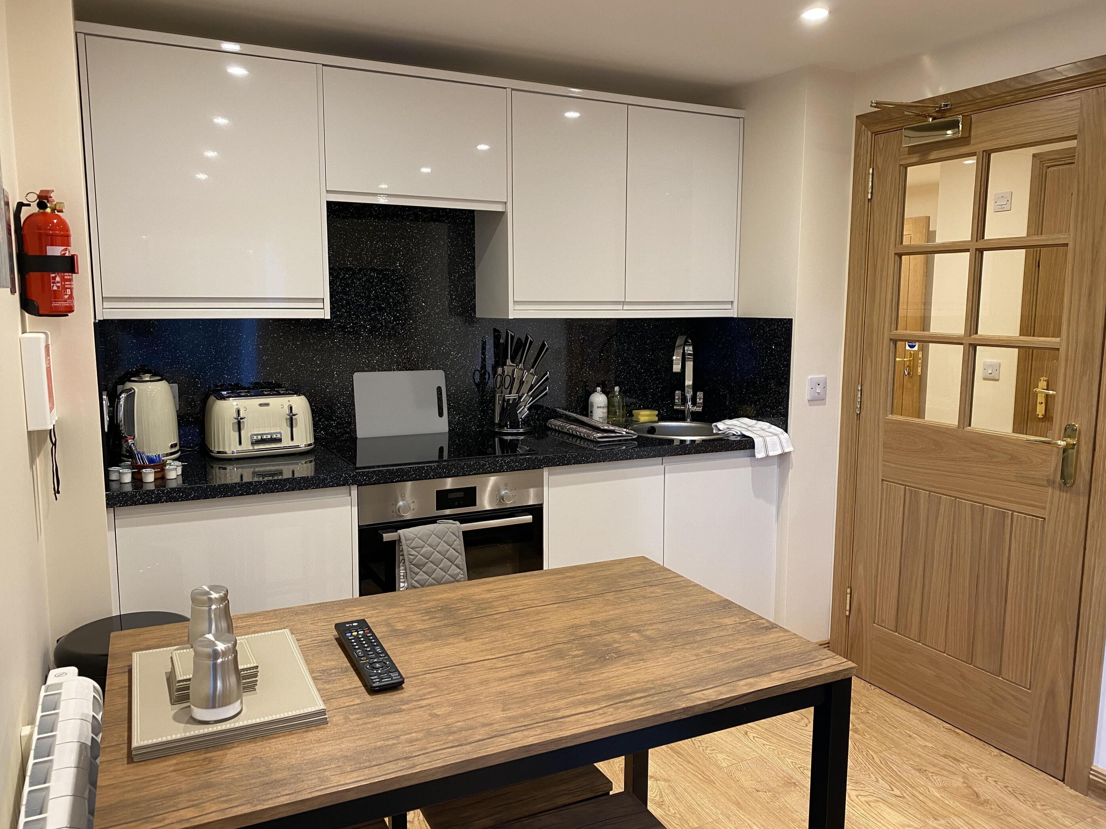 A compact kitchen with white cabinets, a black countertop, and a wooden door.