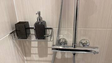 Una doccia con accessori cromati, un soffione a mano e due dispenser di sapone su uno scaffale.