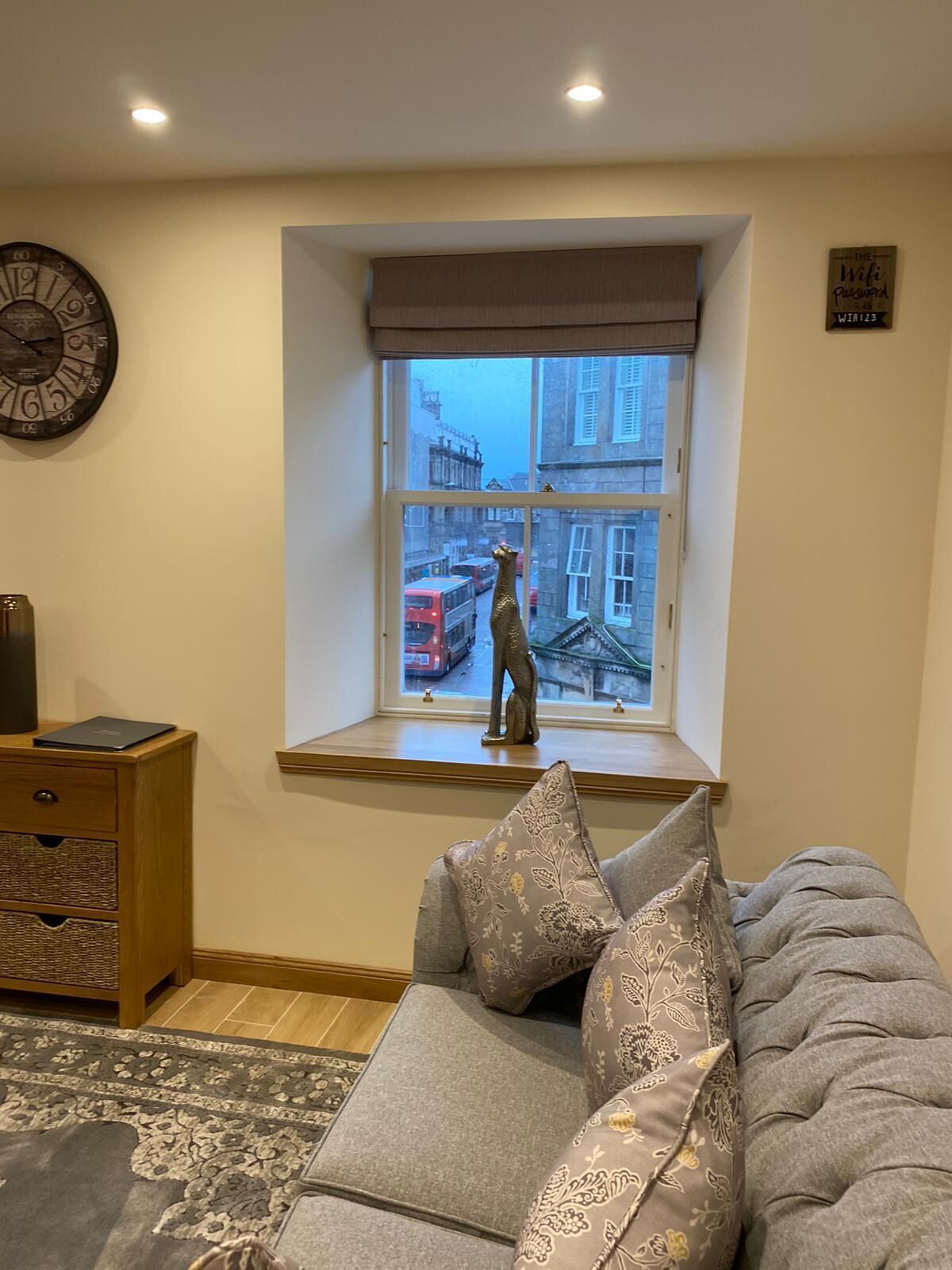 A cozy room with a large window, a clock on the wall, and a statue on the windowsill.