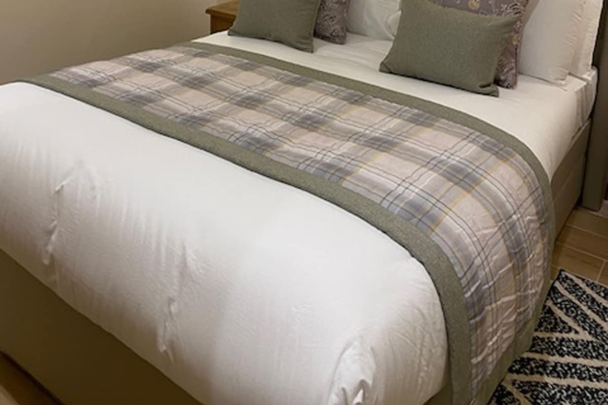 A bedroom with a bed, pillows, a bedside table, and a wall-mounted light.