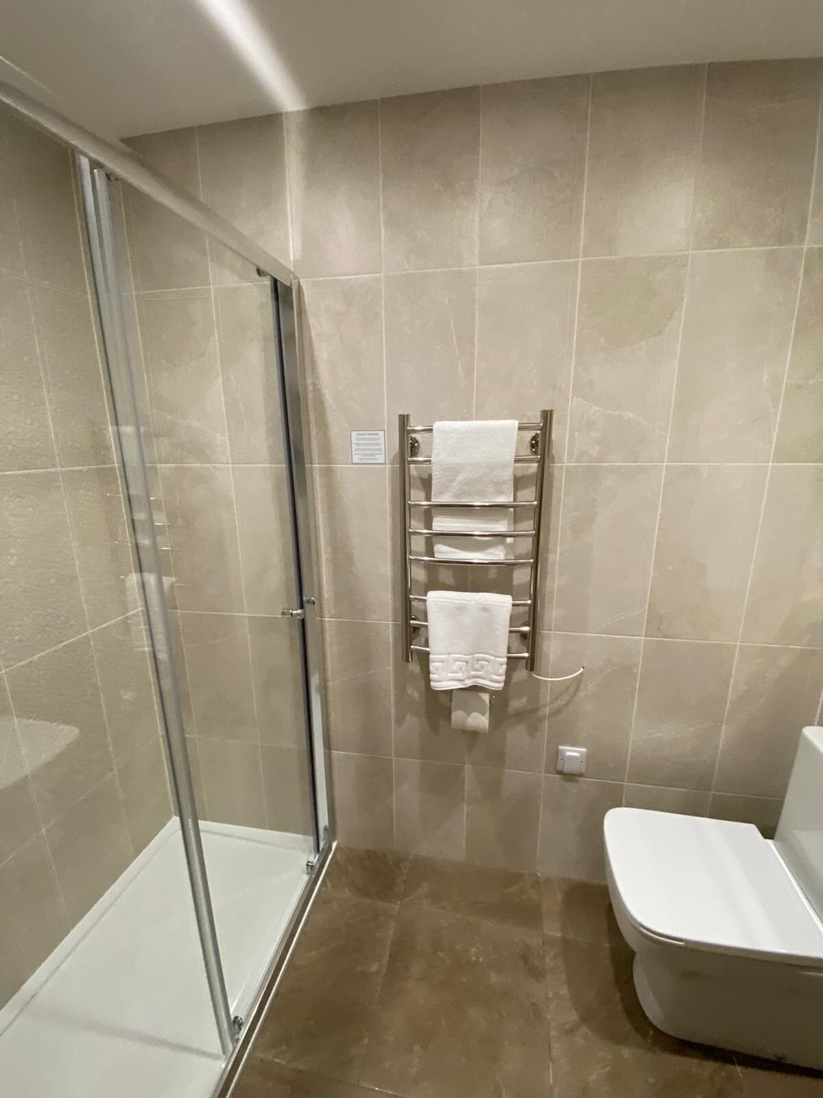 Een badkamer met beige tegels, een douchecabine van glas en een wit toilet.