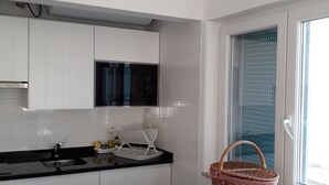 A modern kitchen with white cabinets, a black countertop, a microwave, and a window with blinds. - Cozy Studio in the Historic Center of Cascais! (Cascais)