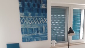 A dining area with a dark wooden table, two white chairs, a blue abstract painting, a white bowl, and a floor lamp. - Cozy Studio in the Historic Center of Cascais! (Cascais)