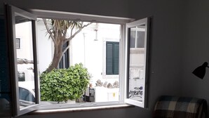 A bedroom with a large window, a chair, a bedside table, and a bed. - Cozy Studio in the Historic Center of Cascais! (Cascais)