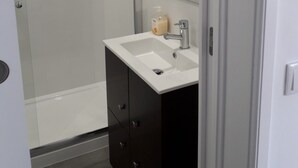 A modern bathroom with a glass-enclosed shower, a white sink with a mirror above it, and dark cabinetry. - Cozy Studio in the Historic Center of Cascais! (Cascais)