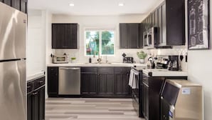 A modern kitchen with dark cabinets, stainless steel appliances, and a window providing natural light. - Brand New Hot Tub & Heated Pool, Perfect Location (Scottsdale)