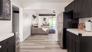 A modern kitchen with dark cabinets, a refrigerator, and a countertop. There is a dining area with a table and chairs in the background. - Brand New Hot Tub & Heated Pool, Perfect Location (Scottsdale)