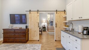 Moderni keittiö, jossa on puinen liukuovi, seinälle asennettu televisio ja kahvinkeitin työtasolla.