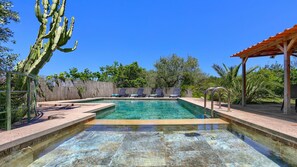 Piscina límpida com espreguiçadeiras e um pergolado de madeira.