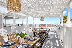An outdoor patio with white railings, tables set for dining, and hanging wicker lamps.