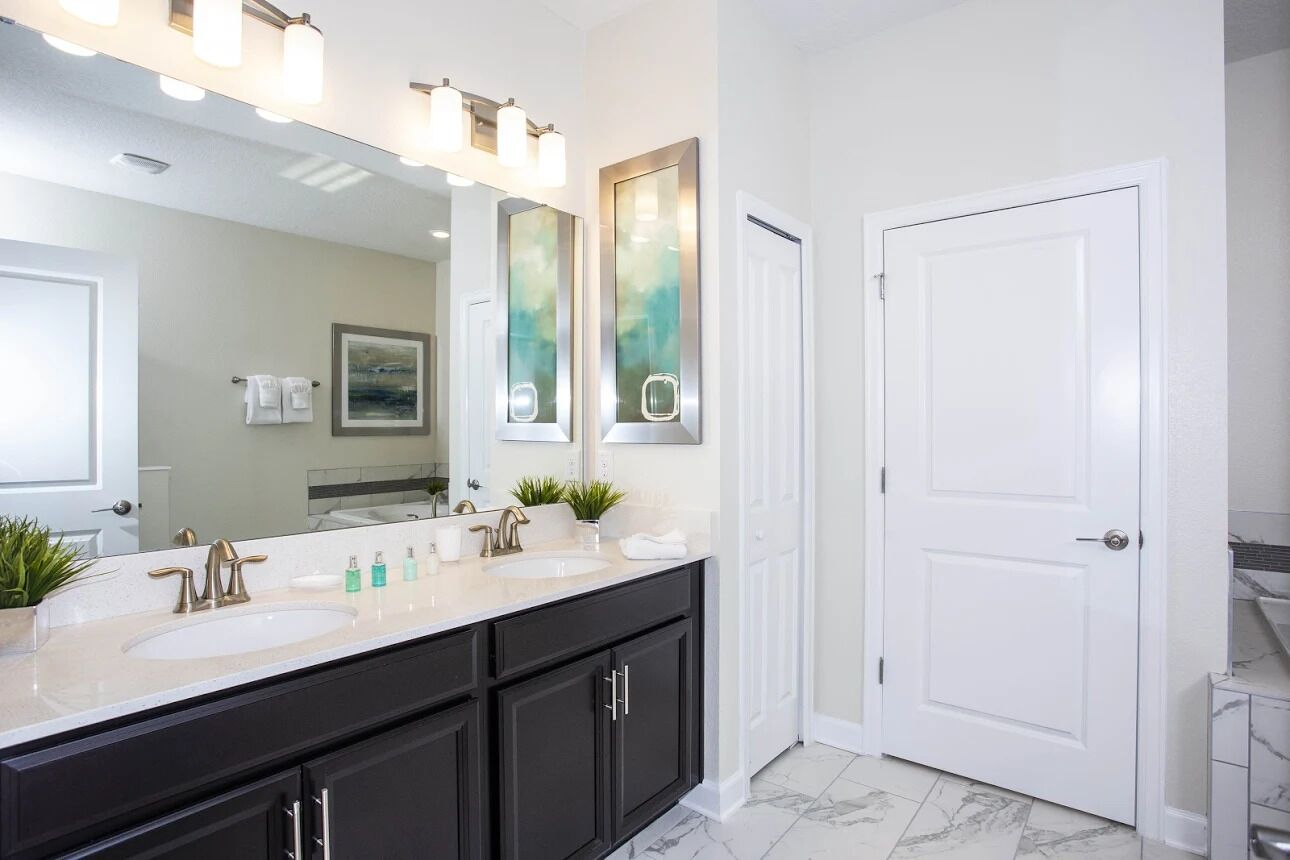 A modern bathroom with two sinks, a large mirror, and a white door.