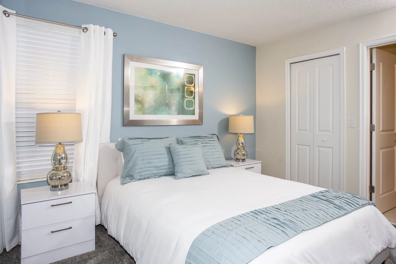 A bedroom with a bed, two bedside tables, a nightstand, a framed abstract artwork, and a door.