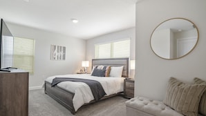 Quarto com cama, mesas de cabeceira, cômoda, espelho redondo e um sofá.