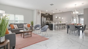 Uma sala de estar moderna com um sofá cinzento, uma mesa de centro e uma área de jantar com mesa posta para seis pessoas.