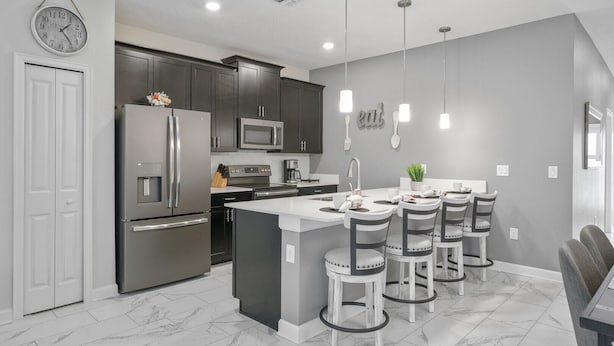 Cozinha moderna com eletrodomésticos de aço inoxidável, uma ilha central com banquetas e esquema de cores cinza.