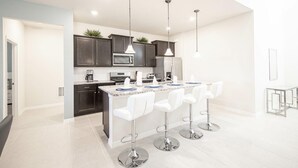 Une cuisine moderne avec des meubles de couleur sombre, un îlot central doté de tabourets de bar, des appareils en acier inoxydable et un éclairage suspendu.