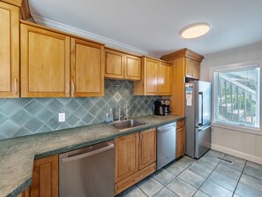 Kitchen features a stainless steel sink, oven, and refrigerator, along with a tiled backsplash and window with blinds.