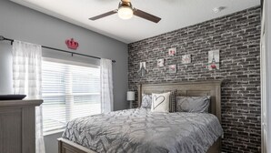 A bedroom with a bed, a dresser, a ceiling fan, and a brick wall. - 230oca - The Retreat at Championsgate (Kissimmee)