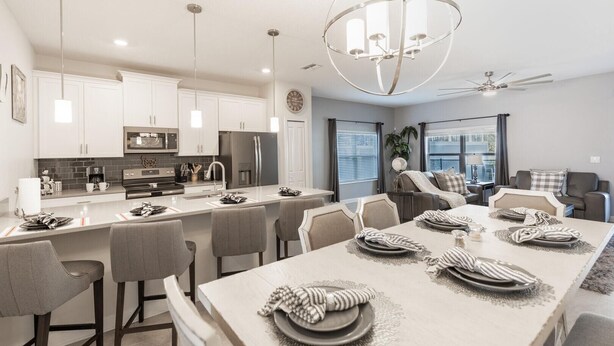 A modern kitchen with white cabinets, stainless steel appliances, and a central island with bar seating. - 230oca - The Retreat at Championsgate (Kissimmee)