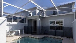 A modern outdoor pool area with a glass enclosure, a seating area with chairs, and a view of the surrounding buildings. - 230oca - The Retreat at Championsgate (Kissimmee)